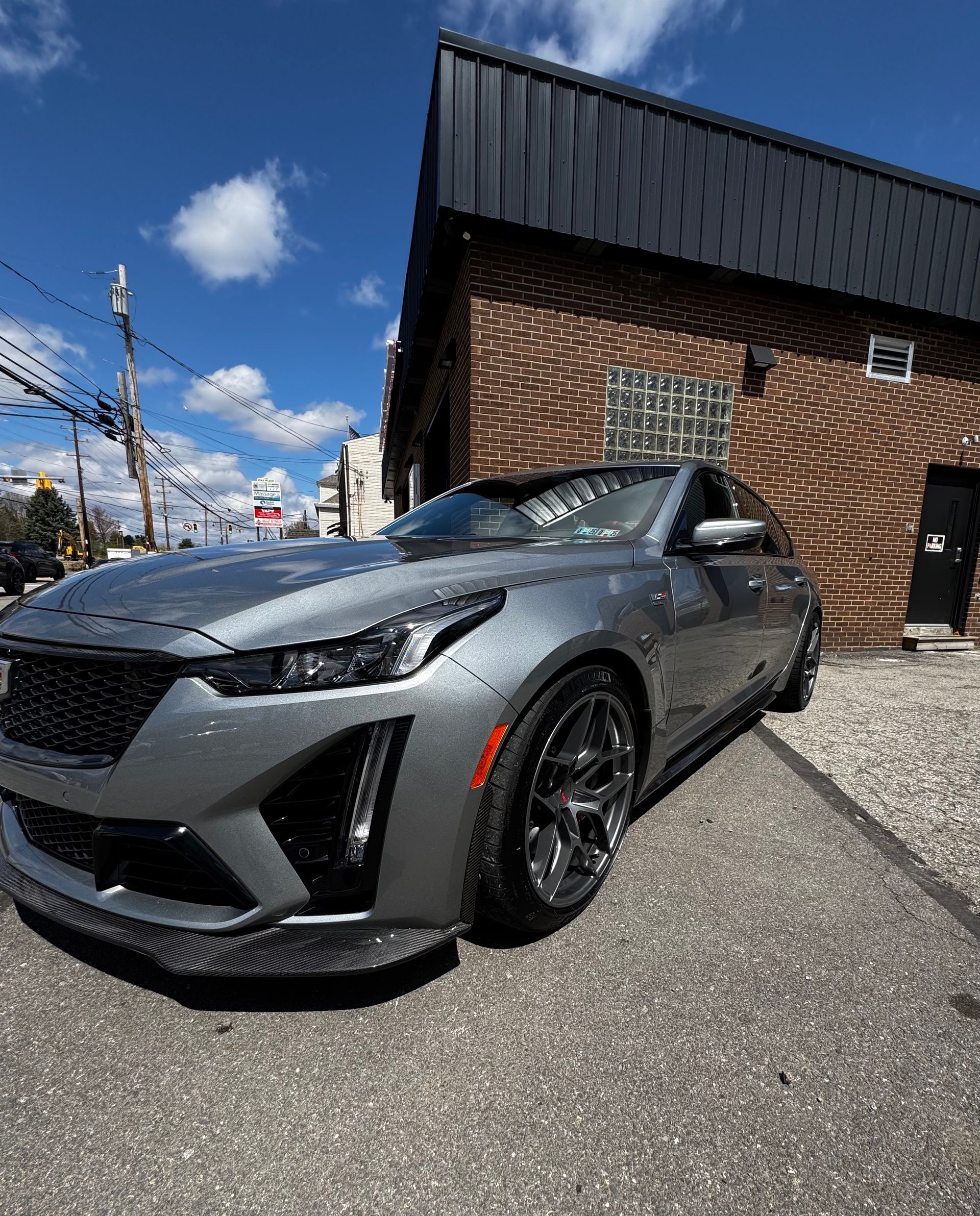 Silver Cadillac sports car parked in front of a brick building on a sunny day.