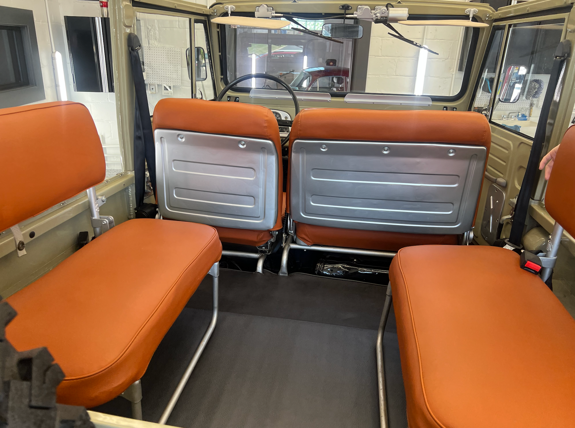Tan and orange interior of a vintage vehicle with bench seats and metal backrests.