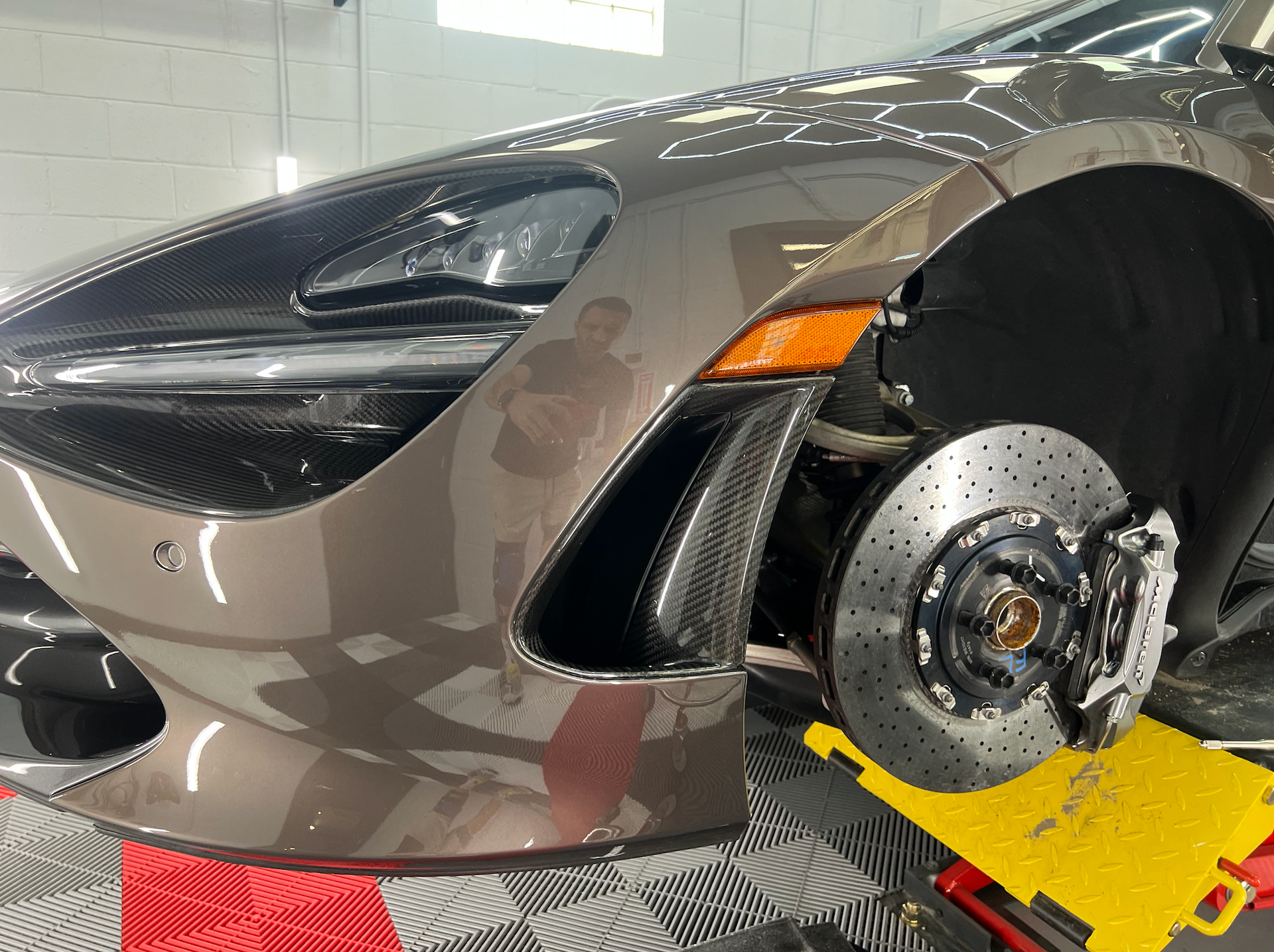 Close-up of a brown McLaren's front end, with the wheel removed, revealing brakes.