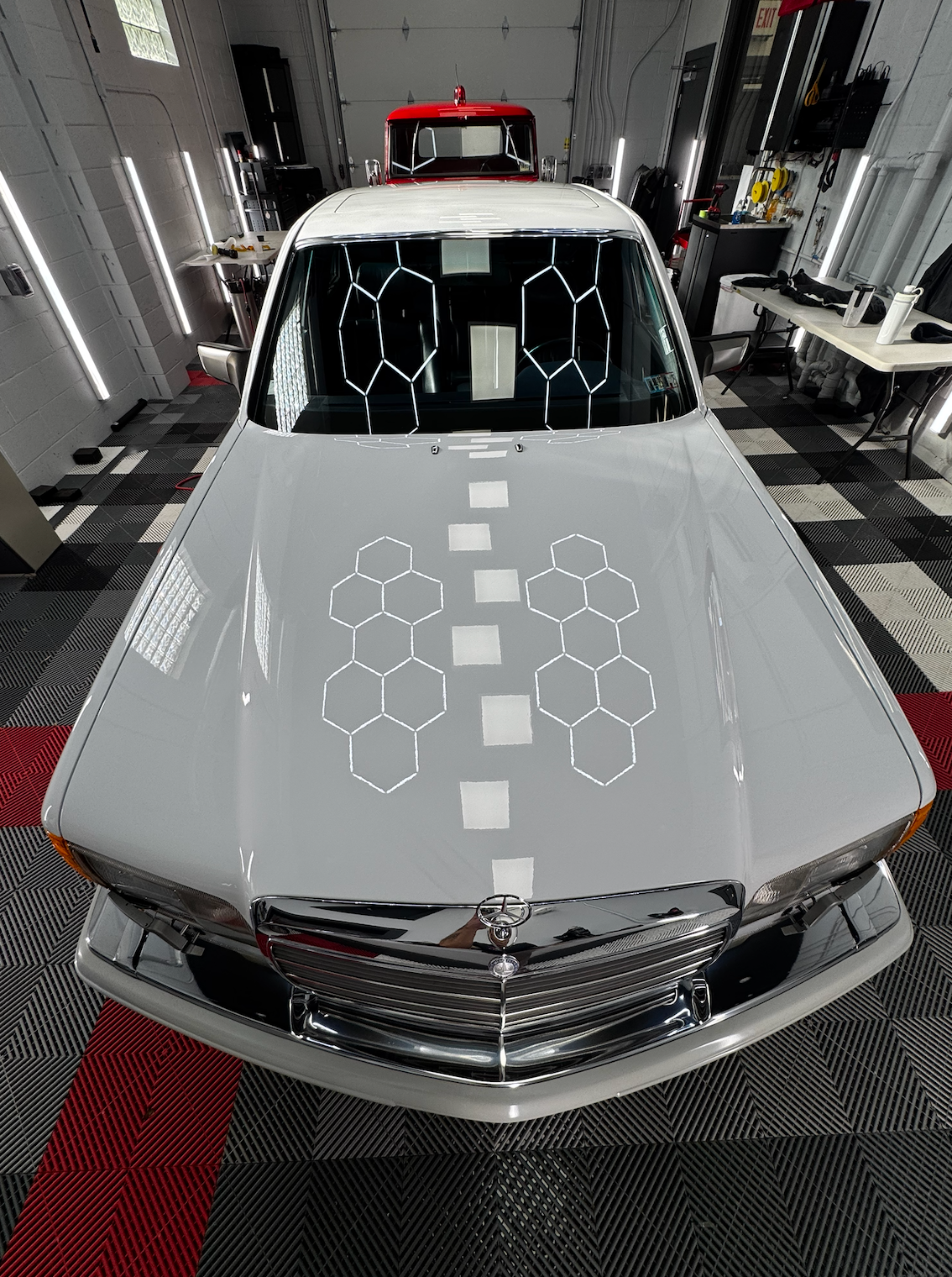 White car in a well-lit garage, hood reflecting light, a grid of hexagons on the hood.