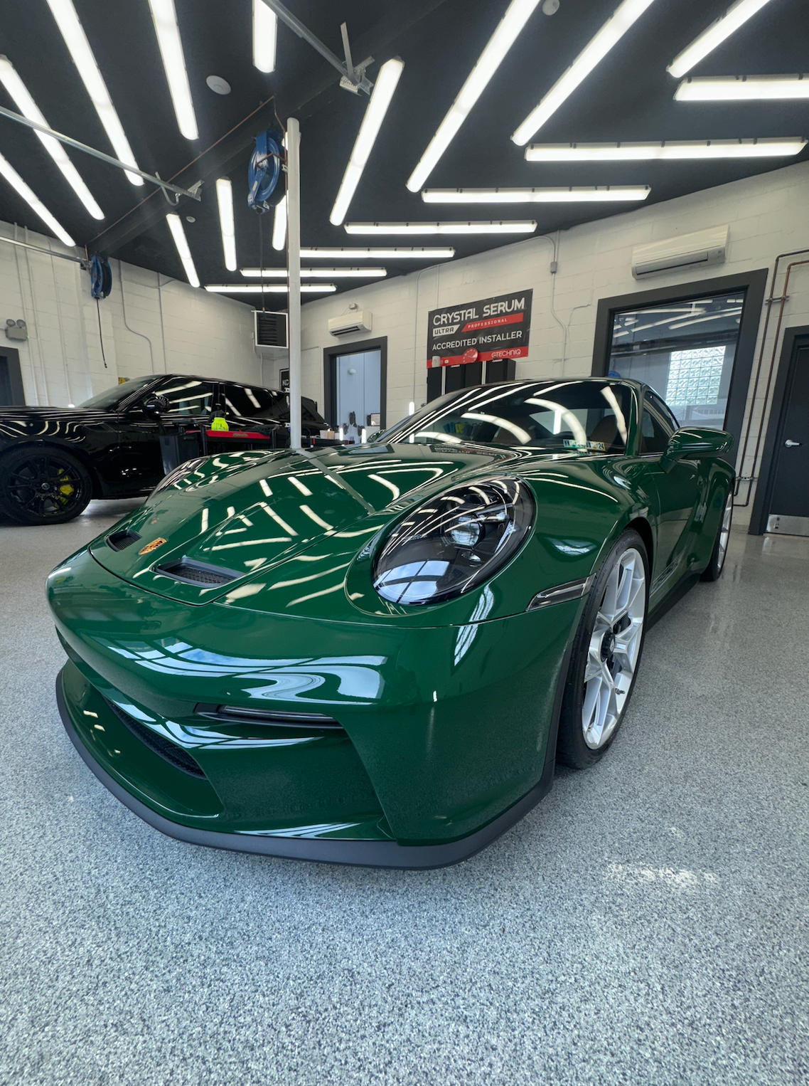 Green sports car parked in a well-lit garage, with a black car in the background.