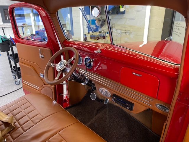 Interior of a classic red truck with tan leather seats and dashboard.