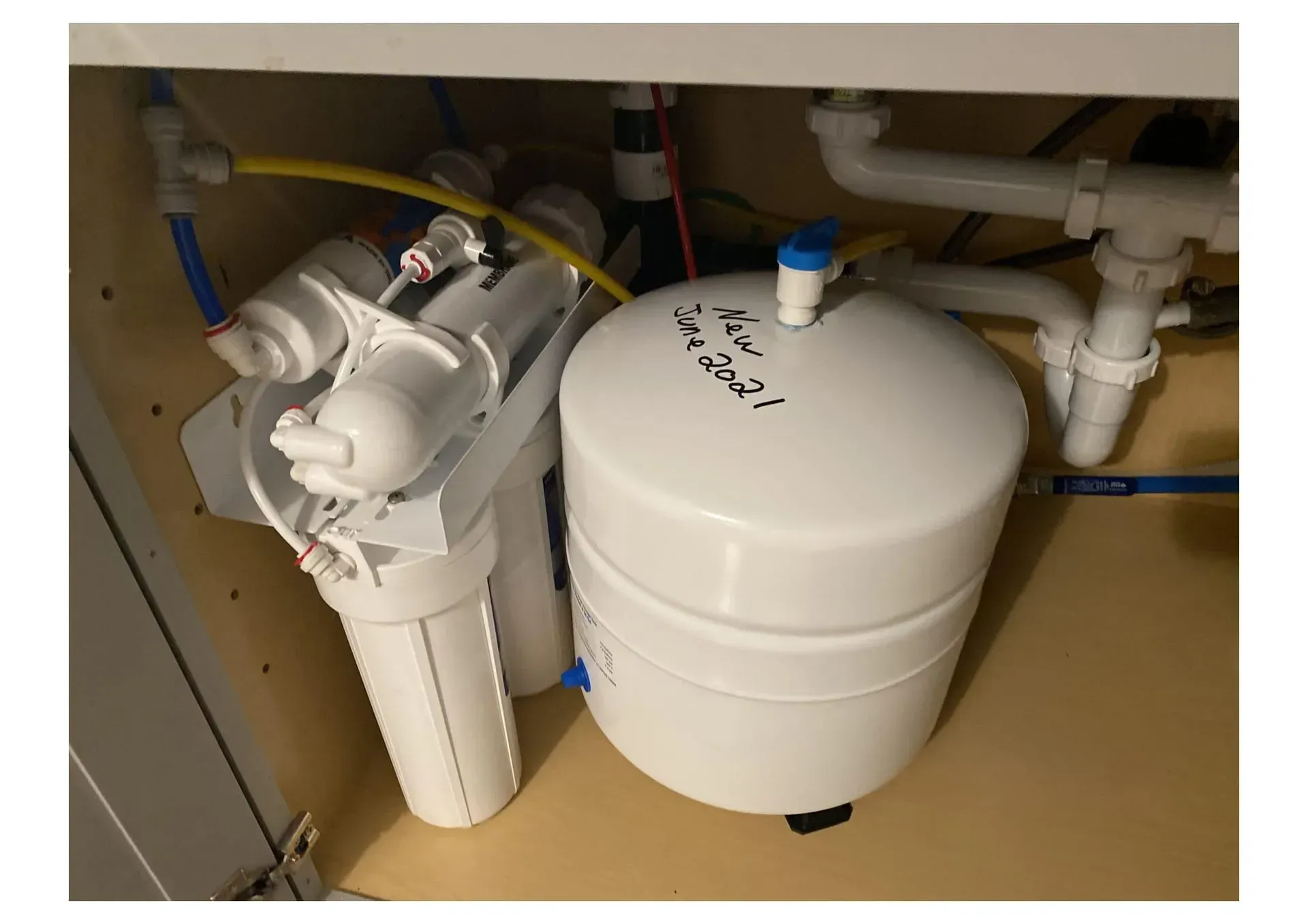 Reverse osmosis water filtration system under a sink. White filter canisters and storage tank.