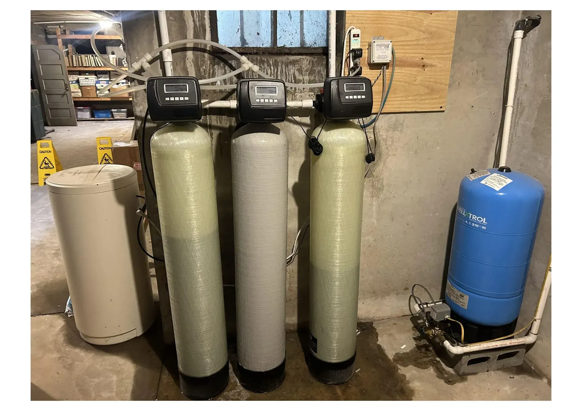 Water filtration system with three tall cylindrical tanks and a blue pressure tank in a basement.