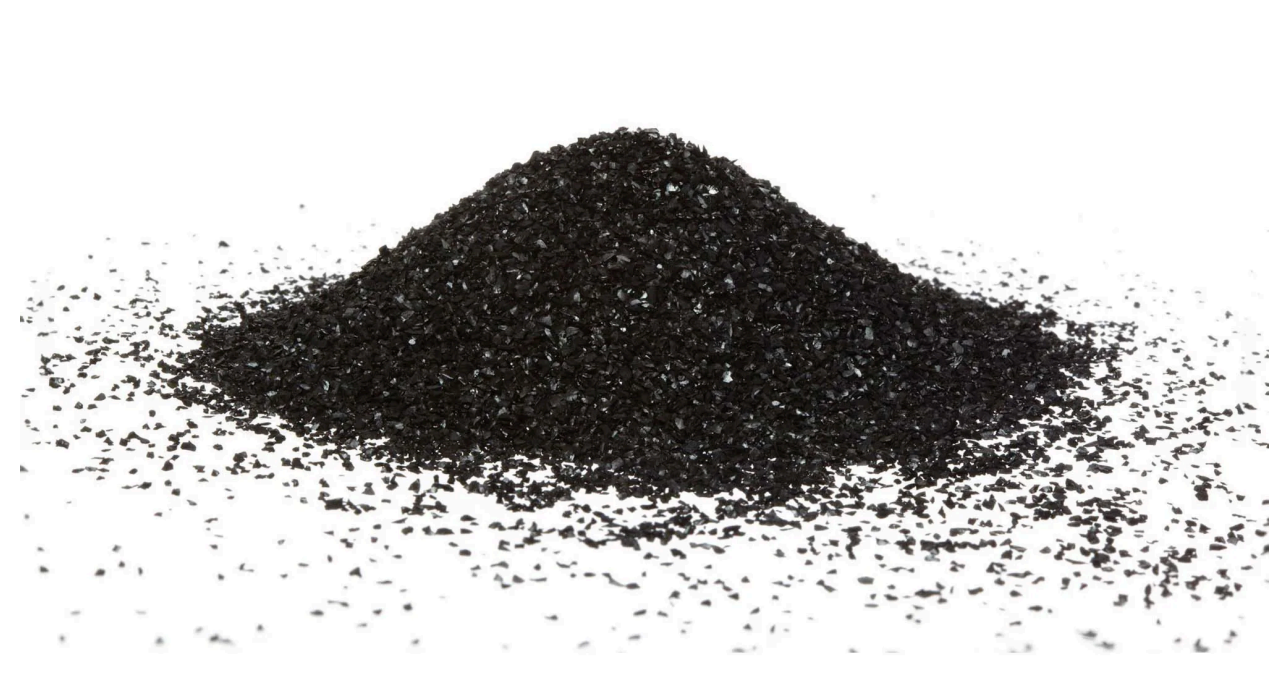 Pile of dark gray granular material, likely activated carbon, on a white surface.