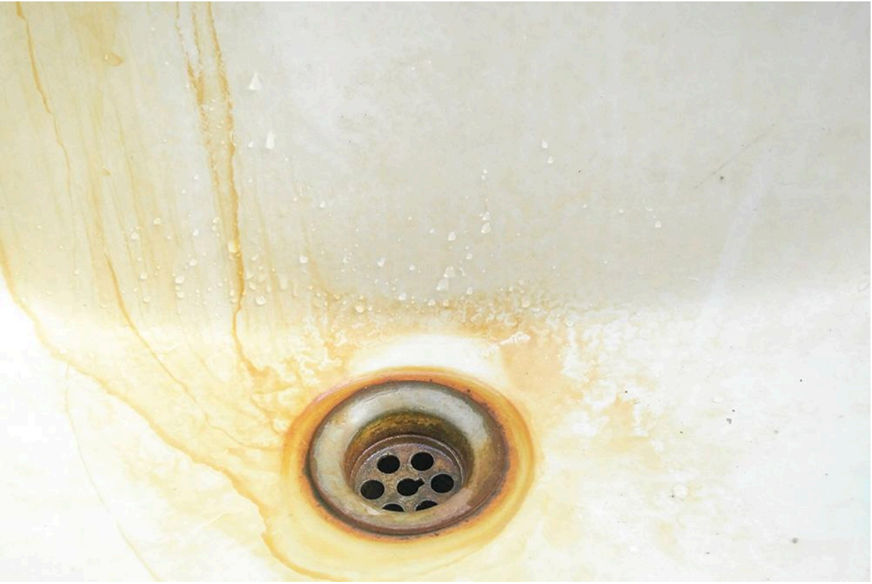 A close-up of a dirty sink drain with rust stains surrounding it.