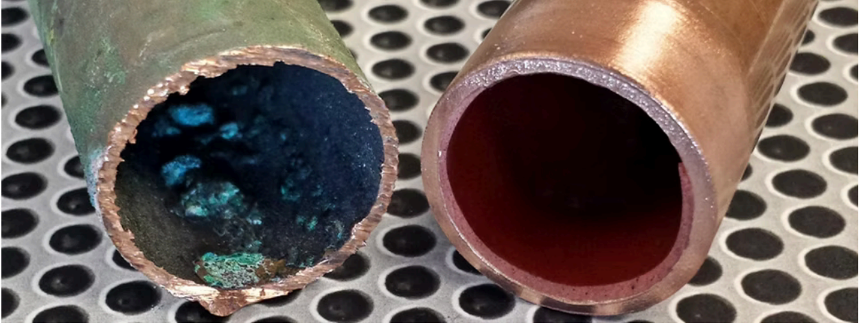 Cross-section of copper pipes: one corroded with blue deposits, the other clean and copper-colored.