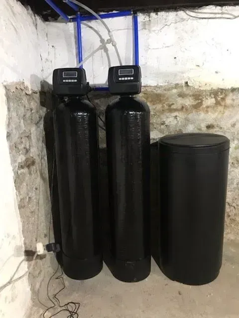 Two black water filtration tanks with digital displays, and a salt tank in a basement corner.