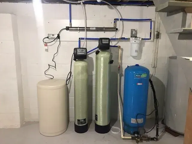 Water filtration system in a basement; includes tanks, filters, and UV light. Blue, beige, and gray colors.