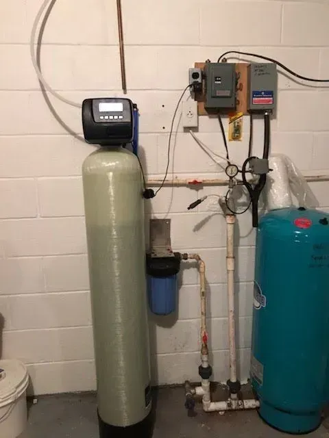 Water softener system and pressure tank in a basement, with control panel, filters, and piping.