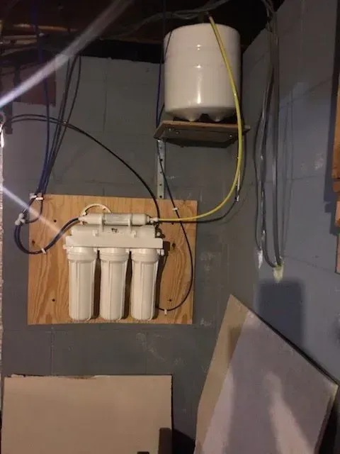 Reverse osmosis water filtration system mounted on a plywood board in a basement.