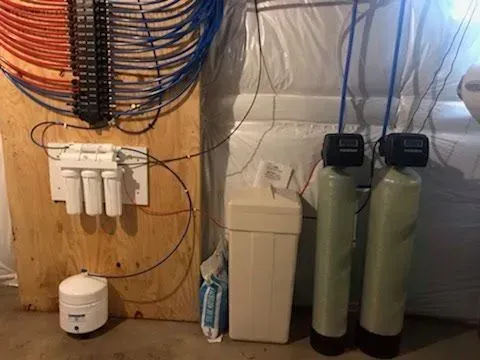 Water filtration and softening system in a basement setting; includes tanks, filters, and pipes.