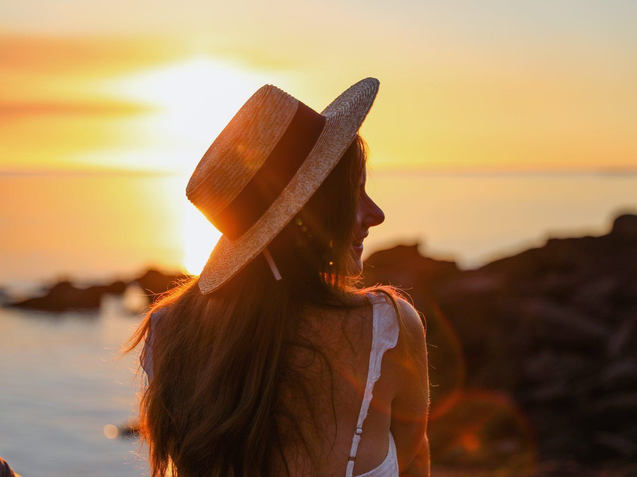 Young woman in hat sitting and looking at sunset