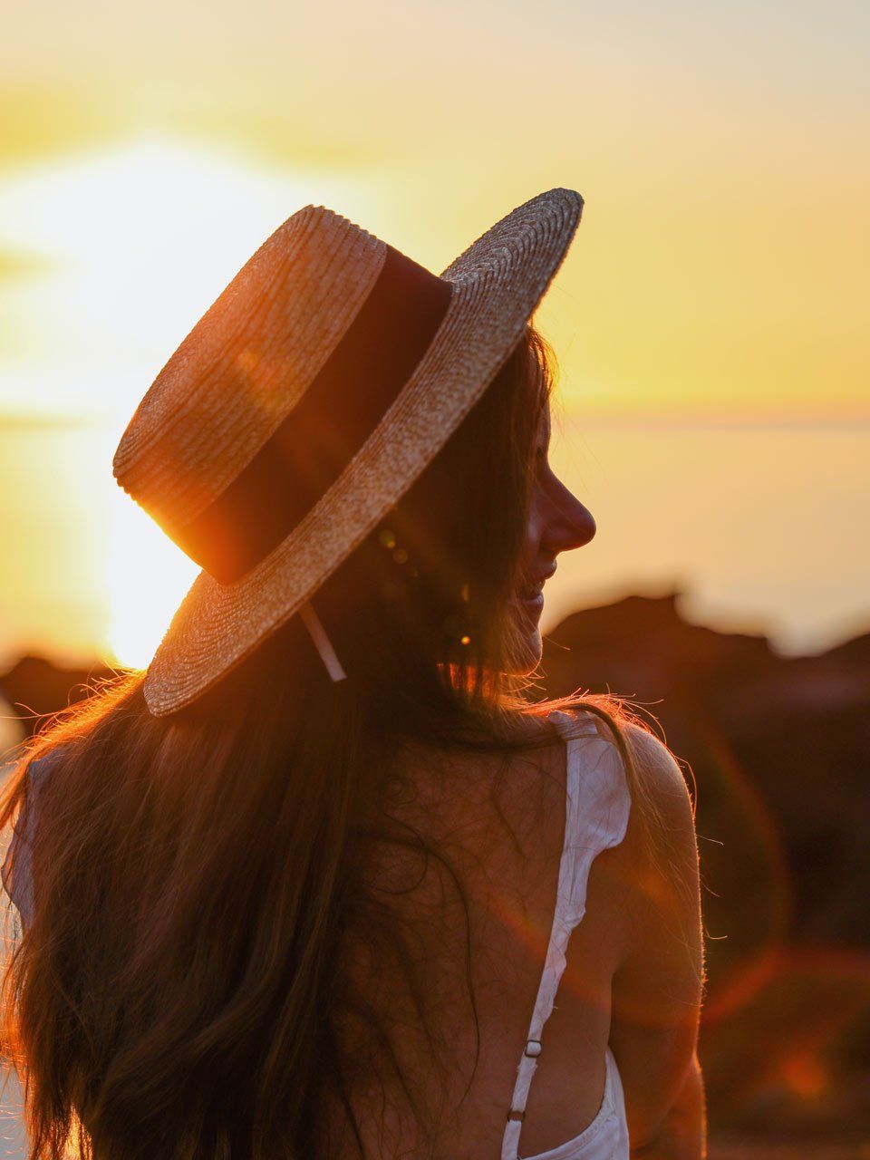 Young woman in hat sitting and looking at sunset