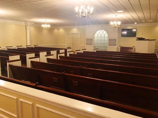 Empty church auditorium with rows of wooden pews, chandeliers, and a small stage.