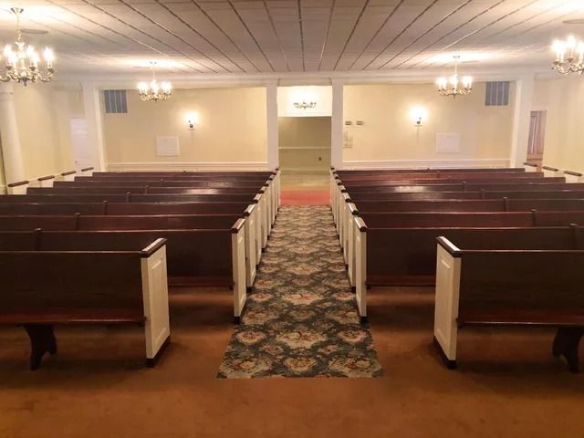 Interior of a church sanctuary with rows of pews, a patterned carpet, and chandeliers.