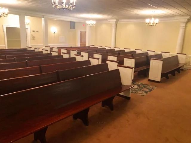 Rows of wooden pews in a chapel. Beige walls, orange carpet.