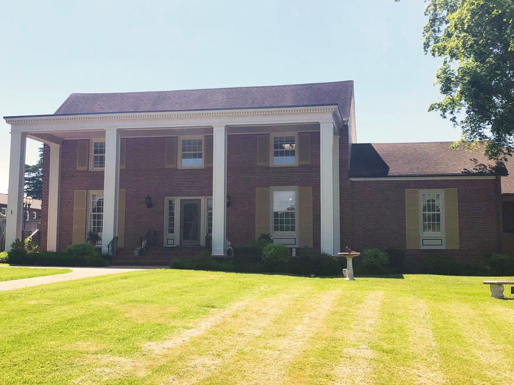 Red brick house with white columns, light green shutters, and lawn.