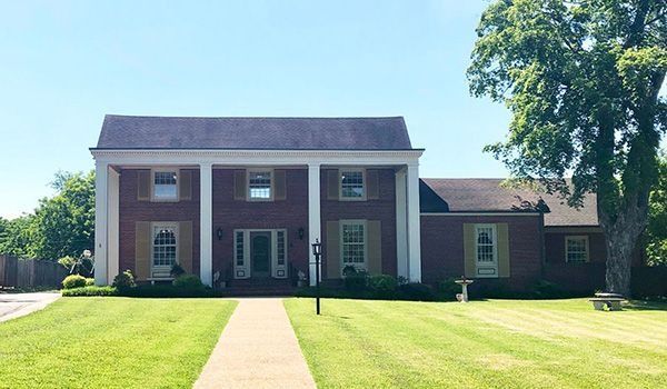 Brick home with white columns, symmetrical facade, green lawn, clear blue sky.