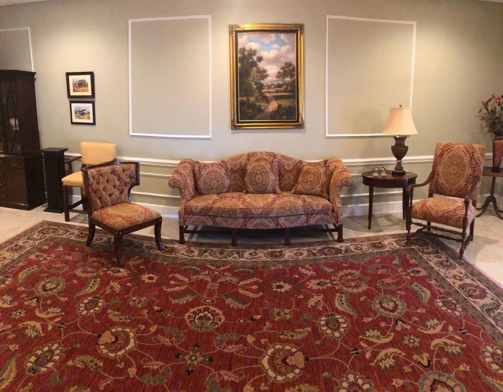 Living room with ornate furniture, landscape painting, and red patterned rug.