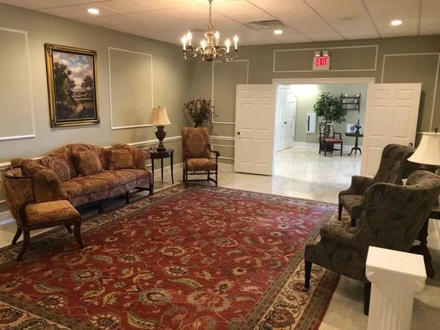 Formal room with ornate furniture, red rug, and exit sign. Light green walls and a chandelier.