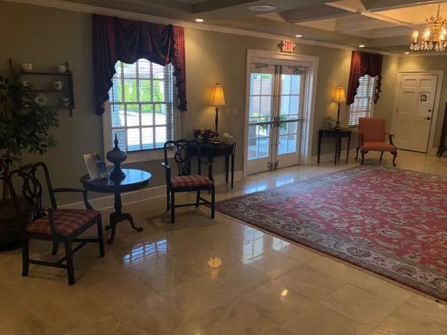 Elegant waiting area with red rug, chairs, tables, and framed window with burgundy drapes.
