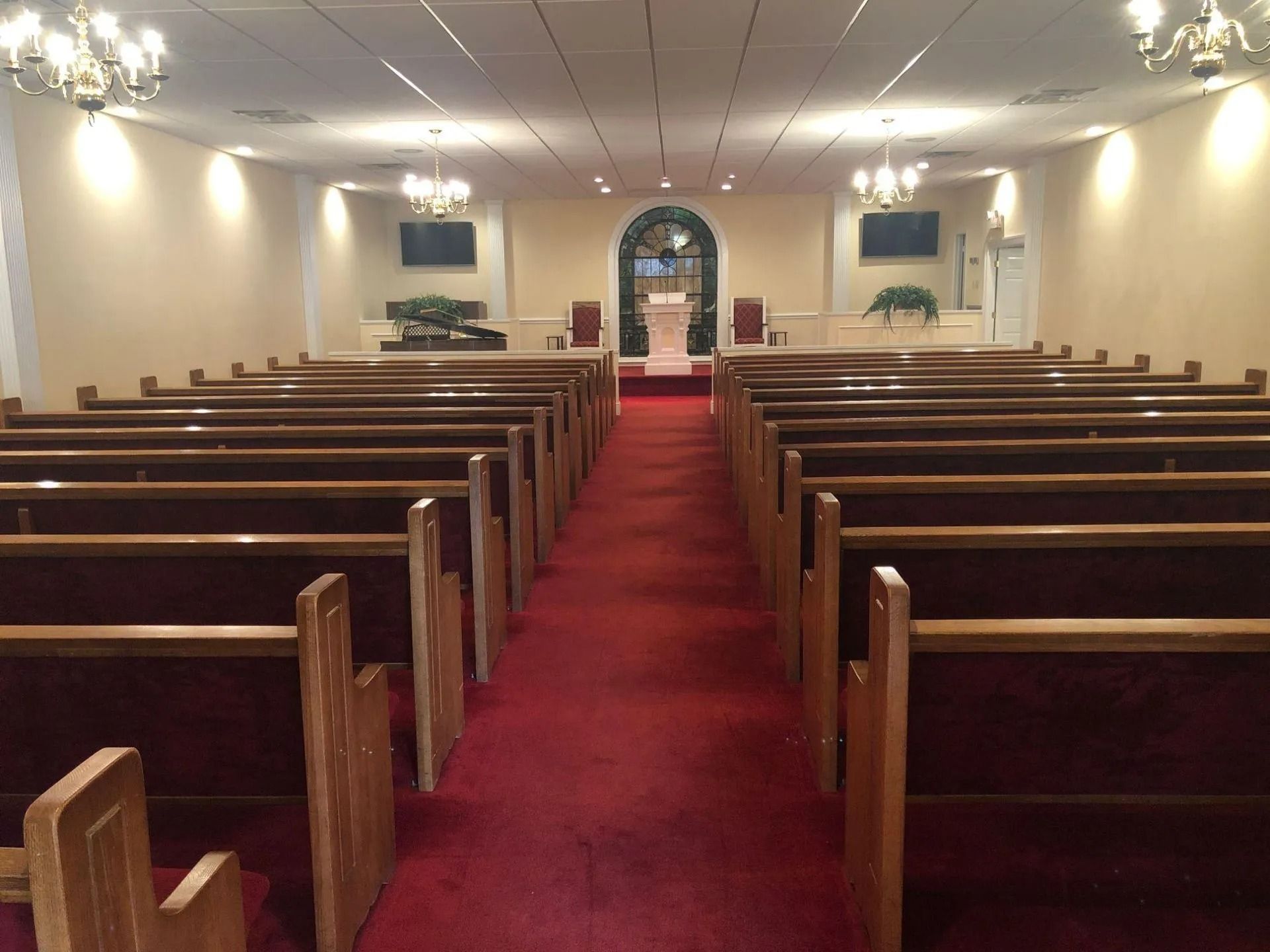 Interior of a chapel with rows of wooden pews, red carpet, and a podium at the front.