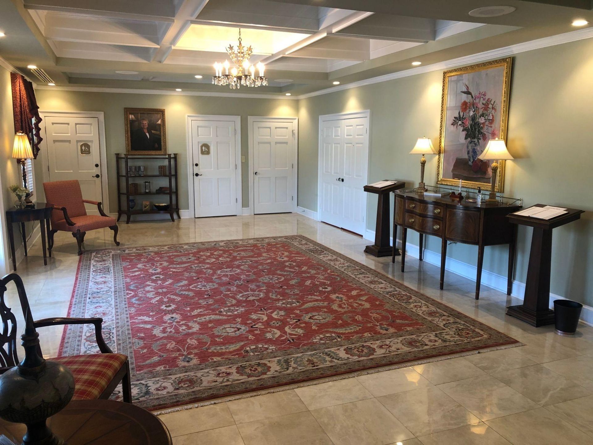 Hallway with red rug, off-white walls, doors, and a decorative chandelier, with furniture and artwork.