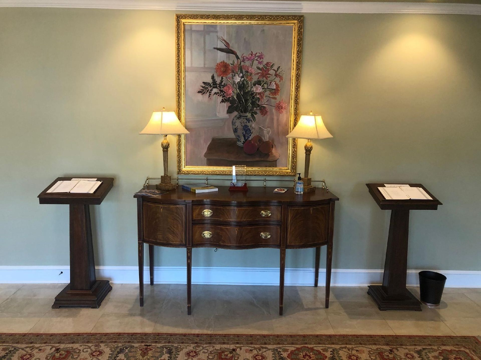 A room with a cabinet, lamps, artwork, and podiums. Soft lighting and green walls.