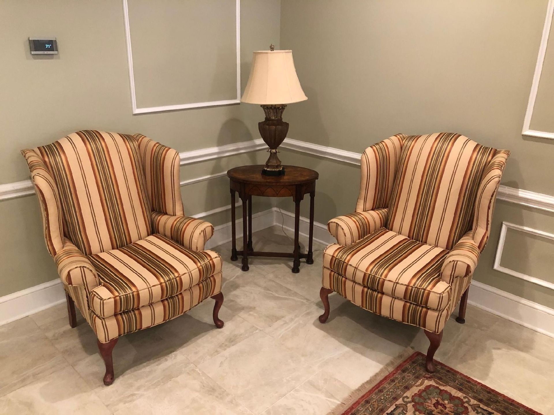 Two patterned wingback chairs face each other with a table and lamp between them.