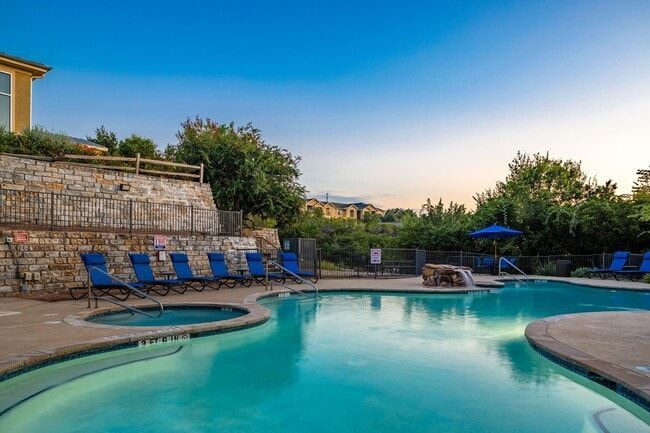 Swimming pool with blue water and lounge chairs; stone wall backdrop under a blue sky.