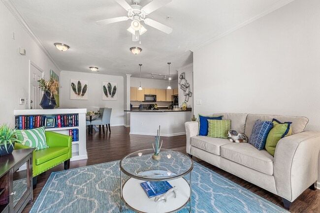 Living room with sofa, green chair, bookshelves, rug, and open kitchen.