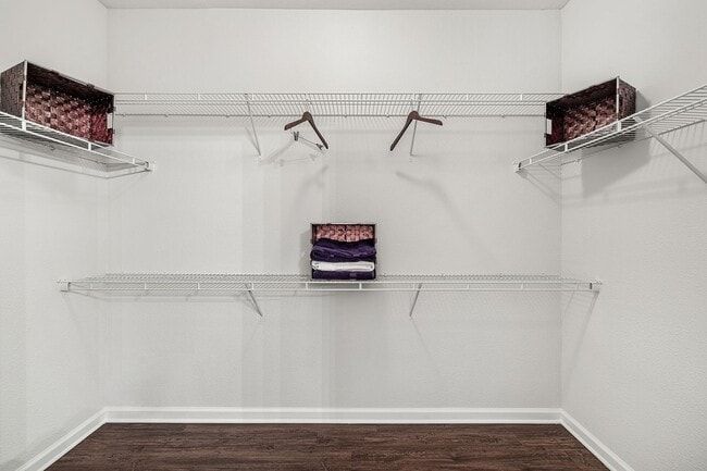 Empty white closet with wire shelving and hangers. Two wooden crates on shelves, stacked clothes.
