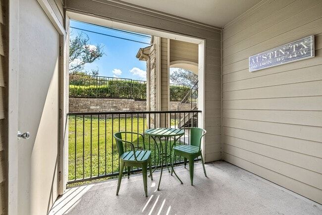 Balcony with green table and chairs, overlooking grassy area with a fence, Austin, TX sign.