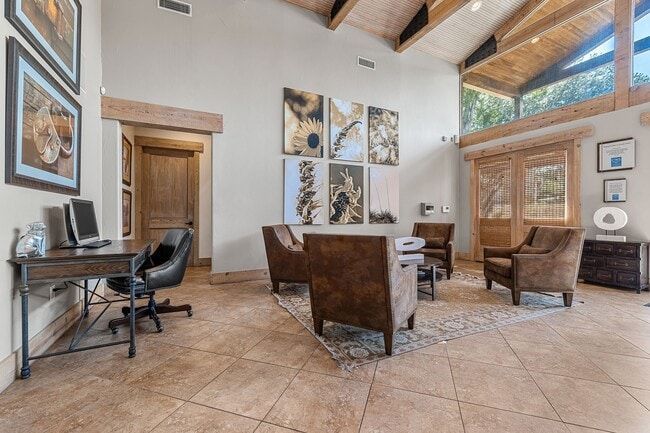 Spacious interior with seating area, desk, artwork, and tall windows; neutral tones.