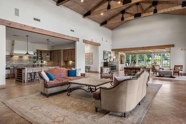 Spacious clubhouse with open kitchen, exposed beams, beige and brown tones, and natural light.