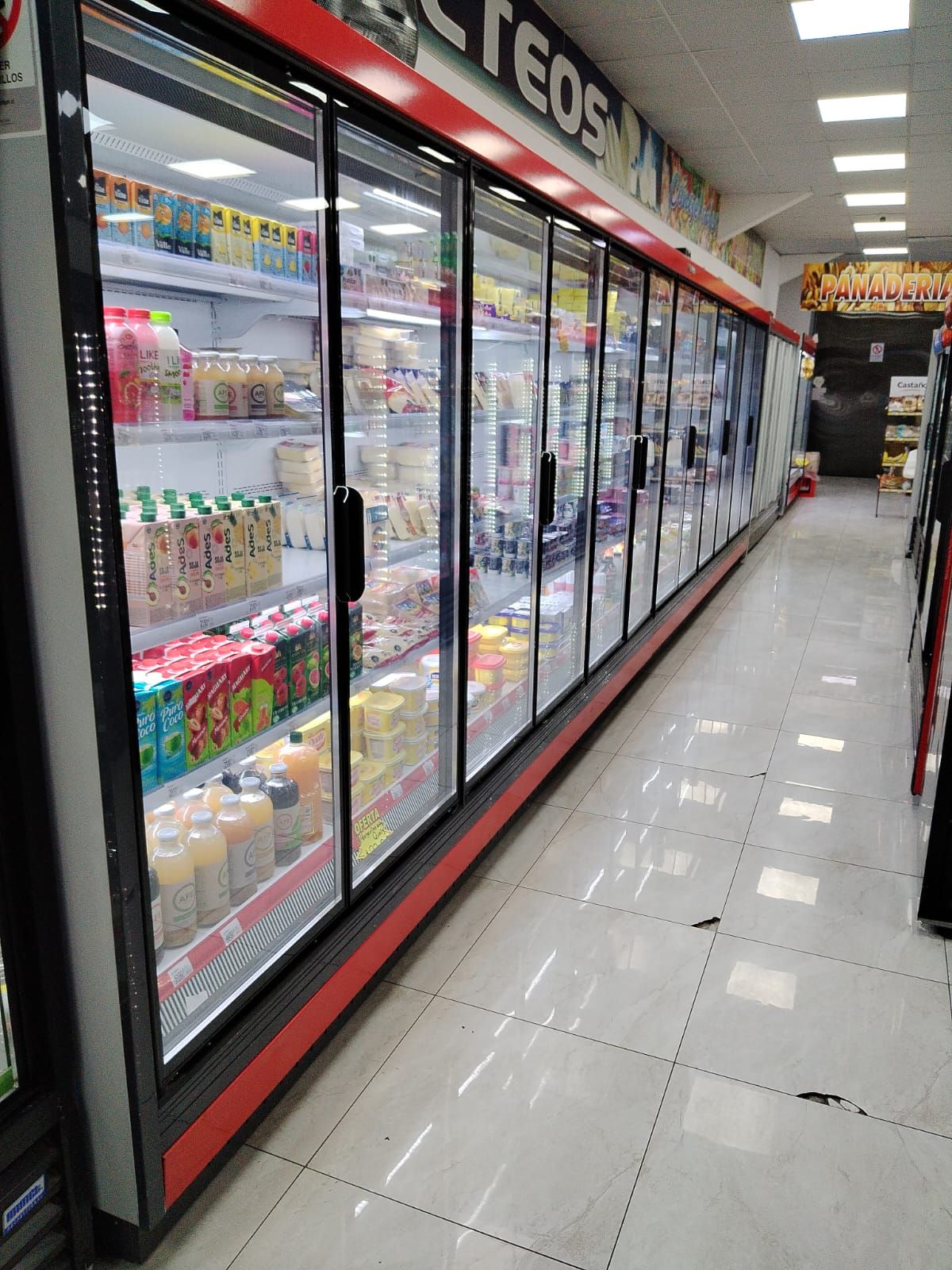 Un pasillo largo de una tienda de comestibles lleno de refrigeradores.