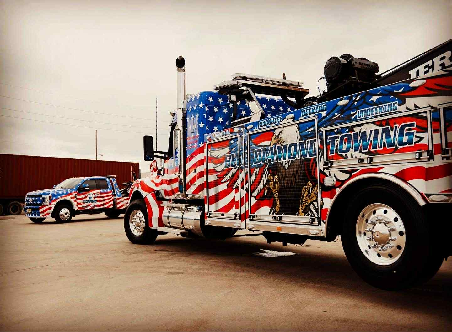 Patriotic-themed tow truck and matching SUV. Both vehicles are painted with the American flag design.