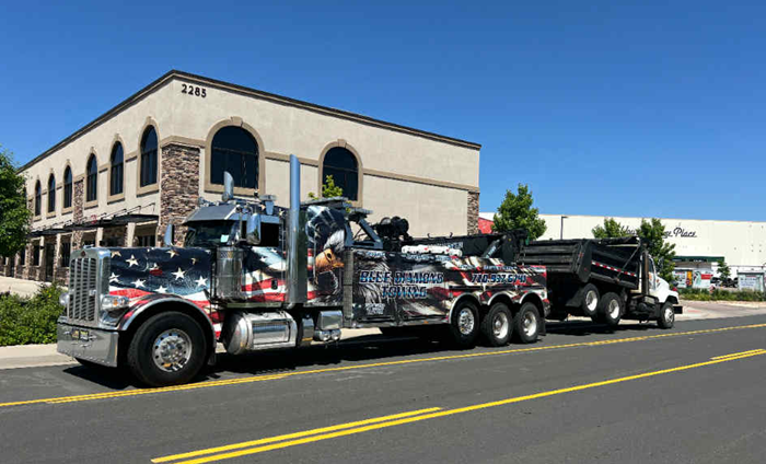 Tow truck with American flag design pulling a dump truck on a sunny day.