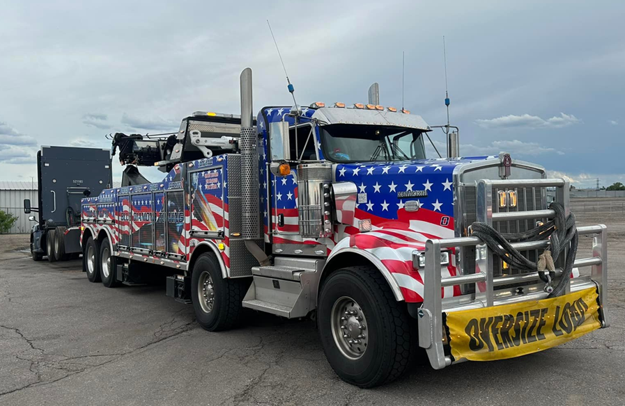 American flag-themed tow truck hauling a semi-truck on a cloudy day.