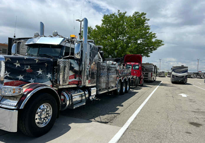 American flag-themed semi-truck with other trucks parked along a road on a cloudy day.