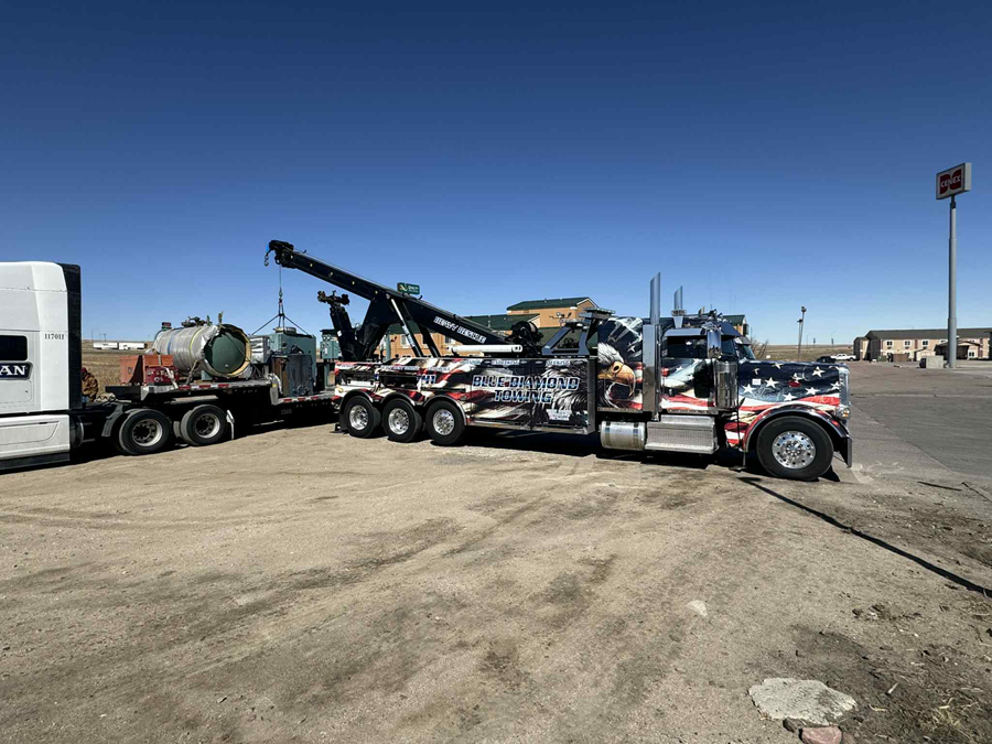 Tow truck with patriotic design towing a tanker trailer on a sunny day.