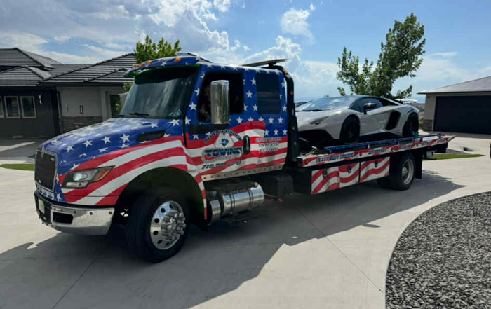 Tow truck with American flag design transporting a white Lamborghini.