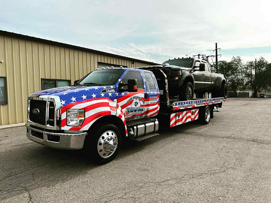Tow truck with American flag design hauling a vehicle. Parked outside a building.