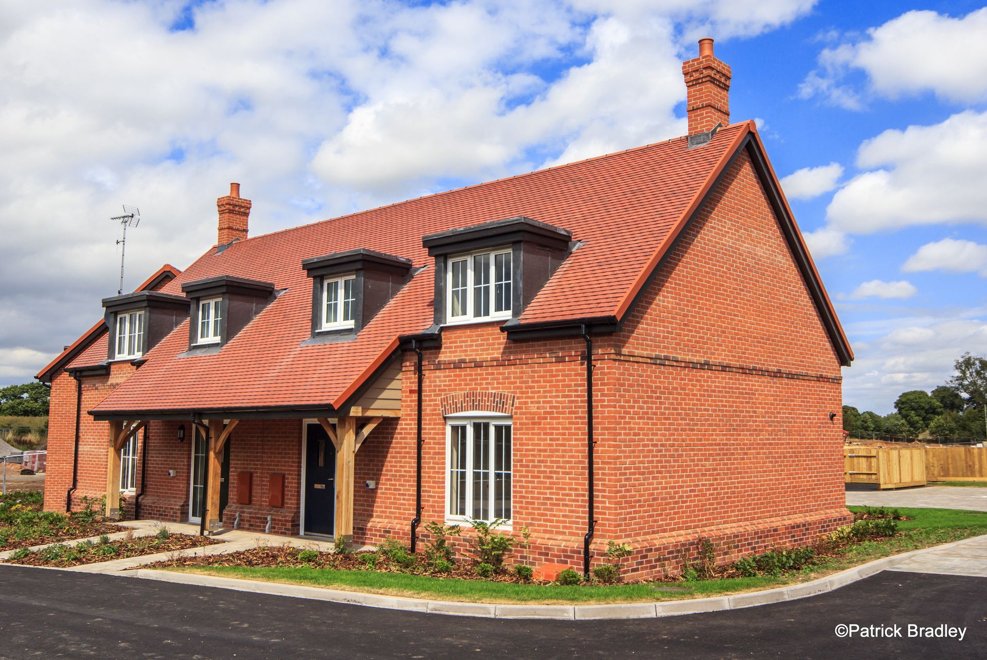 Limetree Village, A brick house with a red tiled roof is sitting on top of a lush green field.