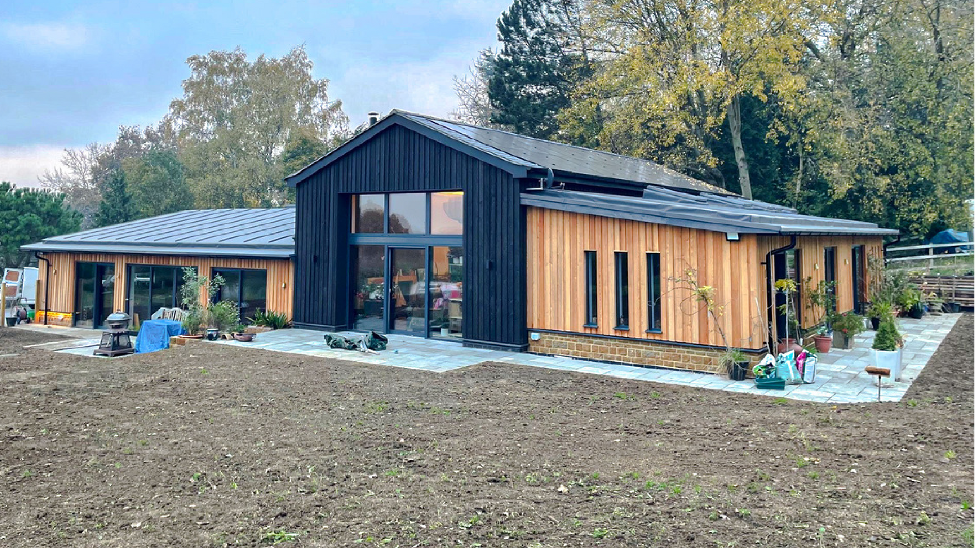 Kingfisher Barn, A large house with a lot of windows is sitting on top of a dirt field.