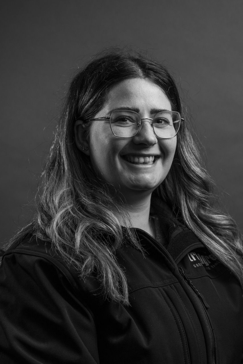 Kayleigh Gorman, awoman wearing glasses and a black jacket is smiling in a black and white photo.