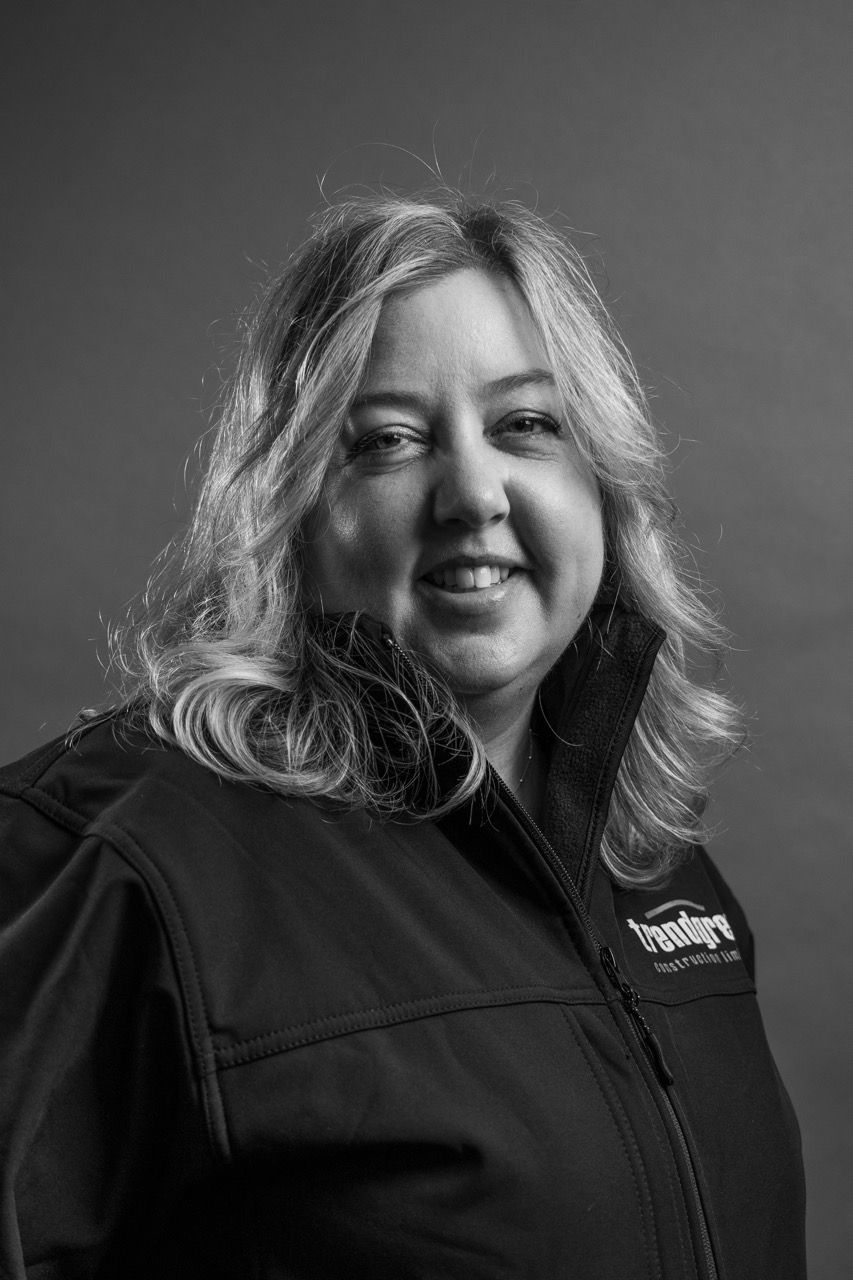 Lisa Henderson, a woman in a black jacket is smiling in a black and white photo.
