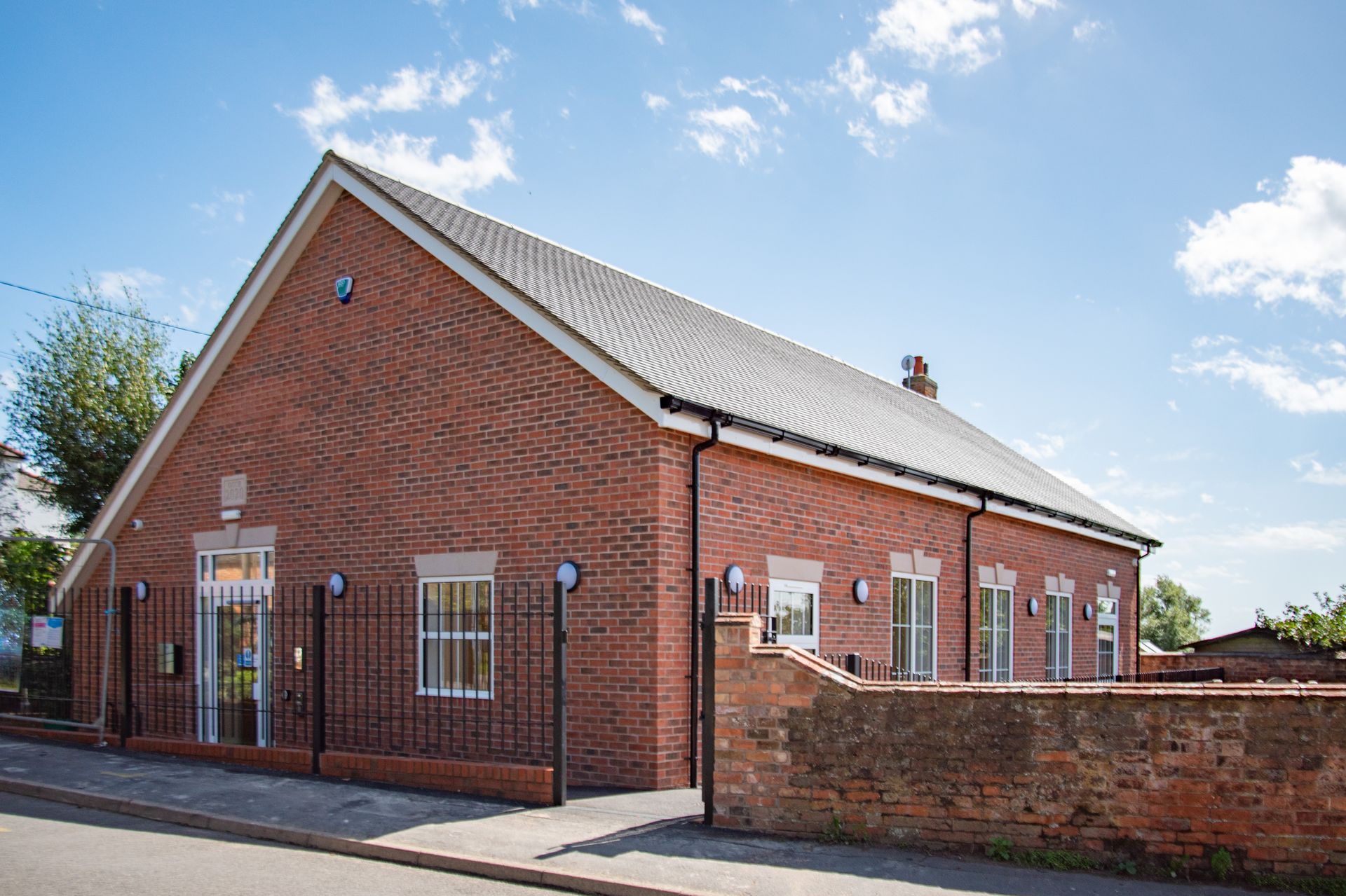 Old School Community Room, A brick building with a fence around it and a blue sky in the background.