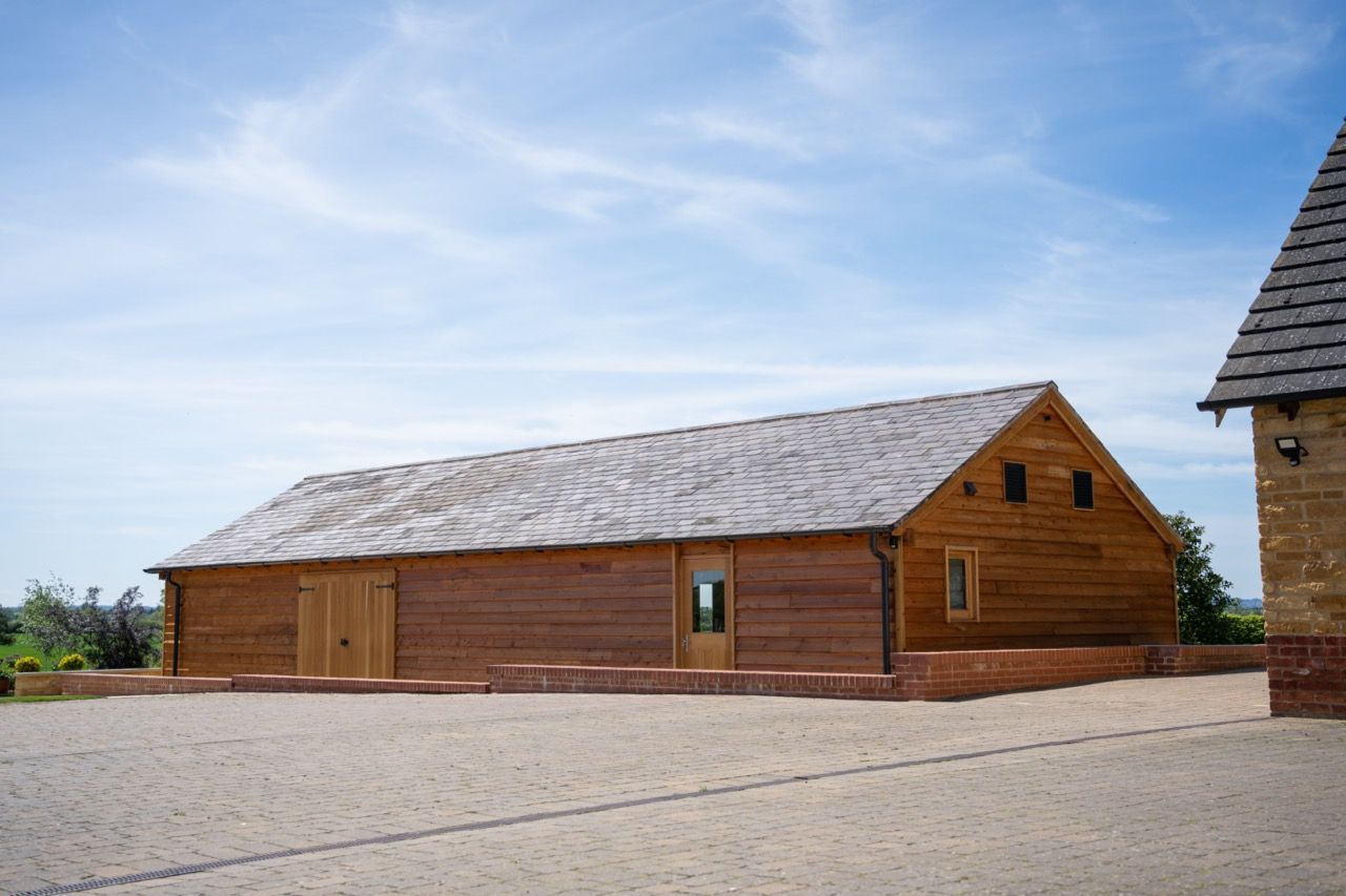 St Dennis Pool House, A large wooden building with a gray roof is sitting next to a stone building.